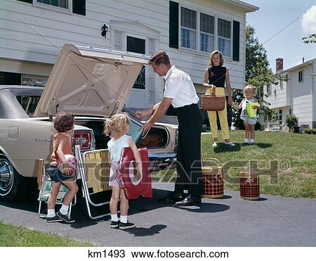 Stock Image - 1960S Family Mother Father Three Daughters Packing Luggage Into Car For Vacation Outdoor. Fotosearch