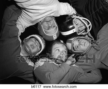 Stock Photo - 1960S Five Boys In Huddle Wearing Helmets & Football Jerseys The View Is From Inside The Huddle Looking Up. Fotosearch