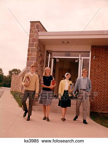 Stock Photography - 1960S Four Teenage Students Walking Out Of Suburban High School Building Carrying Books . Fotosearch
