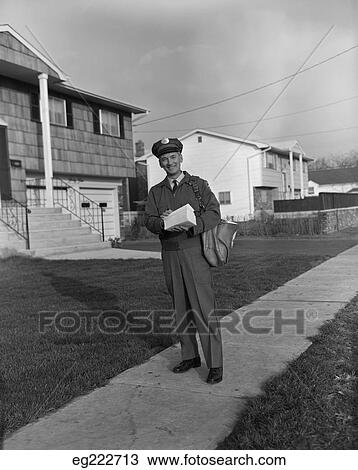 Stock Image - 1960S Mailman Walking Outside Carrying Mail On Suburban Street. Fotosearch