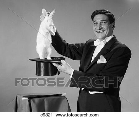 Stock Image - 1960S Man Portrait Smiling Magician Pulling White Rabbit Out Of Top Hat. Fotosearch