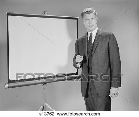 Stock Image - 1960S Man Standing Beside Blank Screen Ready For Presentation Looking At Camera. Fotosearch