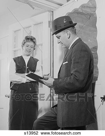 Stock Image - 1960S Man With Clipboard Talking To Woman In Doorway. Fotosearch