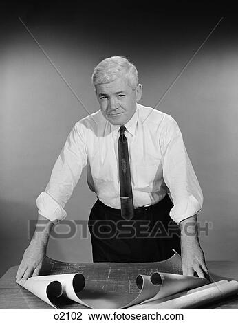 Stock Image - 1960S Middle Aged Man Shirt Sleeves Rolled Up Standing Blueprints On Table . Fotosearch