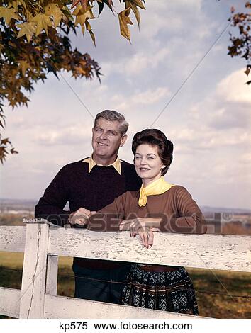 1960S Portrait Couple Husband & Wife Smiling Standing Together Behind White Board Fence Outdoor View Large Photo Image Stock Photography - 1960S Portrait Couple Husband & Wife Smiling Standing Together Behind White Board Fence Outdoor . Fotosearch