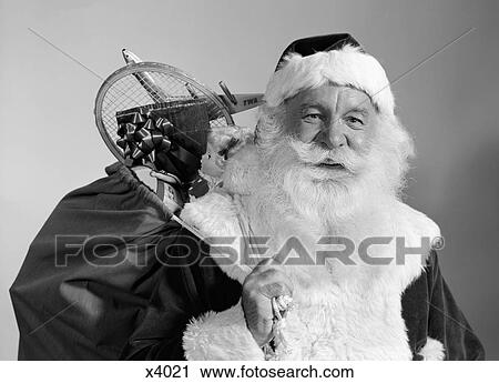 Stock Image - 1960S Portrait Of Smiling Santa Claus With Sack Of Christmas Toy Presents Slung Over His Shoulder. Fotosearch
