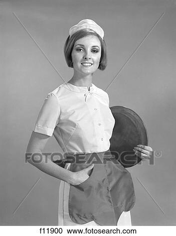 1960S Portrait Smiling Waitress In Uniform Apron And Hat Holding Round Serving Tray Under Arm Looking At Camera View Large Photo Image Stock Image - 1960S Portrait Smiling Waitress In Uniform Apron And Hat Holding Round Serving Tray Under Arm Looking At Camera. Fotosearch