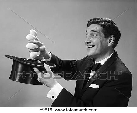Stock Photo - 1960S Profile Magician Man Pulling 4 Eggs Out Of Hat Holding Them Between Fingers. Fotosearch