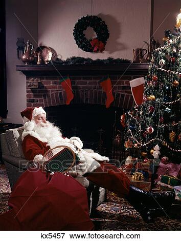1960S Santa Claus Asleep In Chair In Front Of Christmas Tree And Fireplace Indoor View Large Photo Image Stock Photo - 1960S Santa Claus Asleep In Chair In Front Of Christmas Tree And Fireplace Indoor . Fotosearch