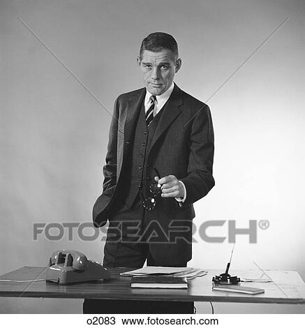 1960S Serious Businessman Three Piece Suit Standing Behind Desk Gesturing With Glasses View Large Photo Image Stock Image - 1960S Serious Businessman Three Piece Suit Standing Behind Desk Gesturing With Glasses. Fotosearch