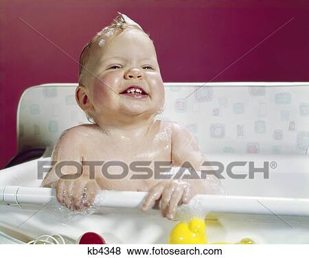Stock Photo - 1960S Smiling Baby Holding On To Side Of Infant Bath . Fotosearch