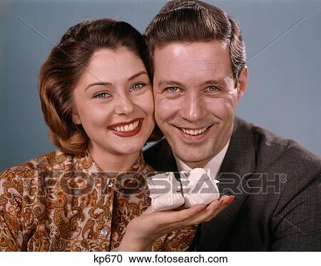 Stock Image - 1960S Smiling Couple Holding Baby Shoes Looking At Camera. Fotosearch