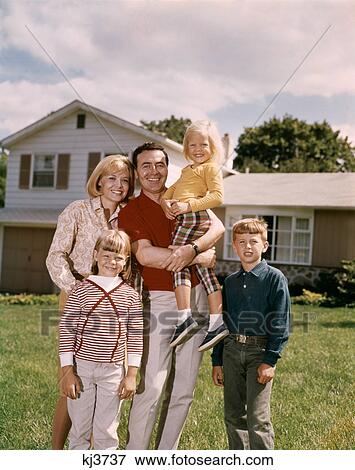 Stock Photo - 1960S Smiling Family Portrait Standing In Front Of A Suburban Split Level House Father Mother Two Daughters And Son . Fotosearch