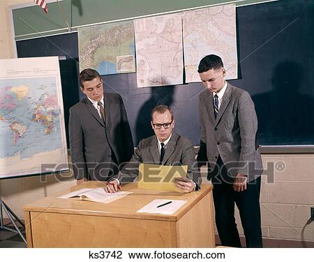 1960S Teacher Sitting At Desk With Boy Students Looking At And Grading Paper Indoor View Large Photo Image Stock Image - 1960S Teacher Sitting At Desk With Boy Students Looking At And Grading Paper Indoor . Fotosearch