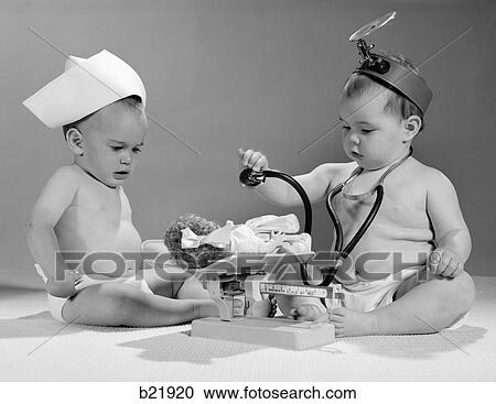 Stock Image - 1960S Two Babies Playing Doctor And Nurse With Doll Studio. Fotosearch