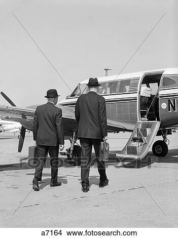 1960S Two Businessmen Walking Together To A Small Private Propeller Airplane Carrying Briefcase View Large Photo Image Picture - 1960S Two Businessmen Walking Together To A Small Private Propeller Airplane Carrying Briefcase. Fotosearch