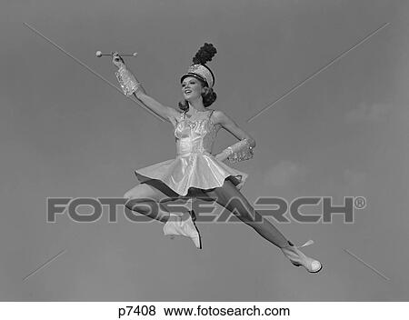 Stock Photo - 1960S Woman Majorette Holding Baton Wearing Short Skirt Uniform Jumping Into The Air. Fotosearch