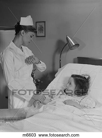 Stock Image - 1960S Woman Nurse Checking Pulse Taking Temperature On Little Girl Patient In Hospital Bed. Fotosearch