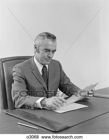 1970S 1960S Businessman Executive Middle Aged Sitting At Desk Reading Papers View Large Photo Image Stock Photo - 1970S 1960S Businessman Executive Middle Aged Sitting At Desk Reading Papers. Fotosearch