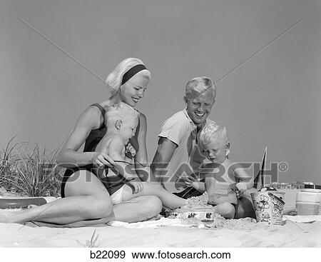 Stock Photo - 1970S 1960S Family Father Mother Twin Sons Playing In Sand On Beach Outdoor. Fotosearch