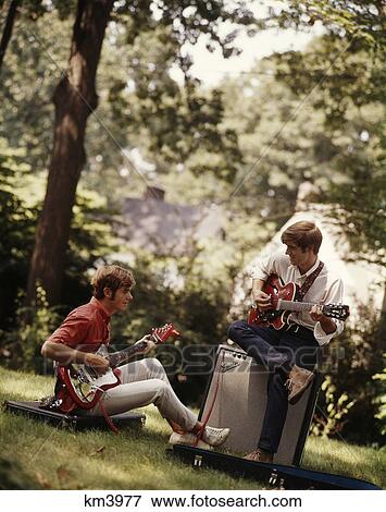 1970S 1980S Two Teenage Boys Playing Electric Guitars Sitting Outdoors With Amplifier And Guitar Cases View Large Photo Image Stock Photo - 1970S 1980S Two Teenage Boys Playing Electric Guitars Sitting Outdoors With Amplifier And Guitar Cases. Fotosearch