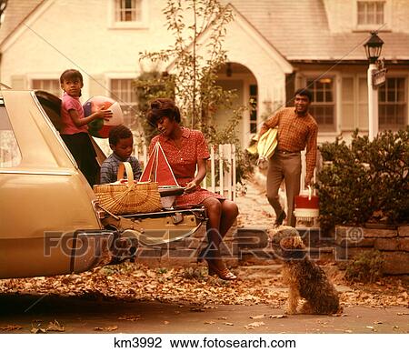 Stock Image - 1970S African American Family Loading Station Wagon Picnic Dog Mother Father Boy Girl Suburban House. Fotosearch