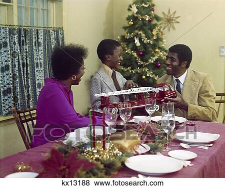 Stock Photo - 1970S African-American Family Mother Father Son Dining Table With Toy Fire Truck Christmas Tree. Fotosearch