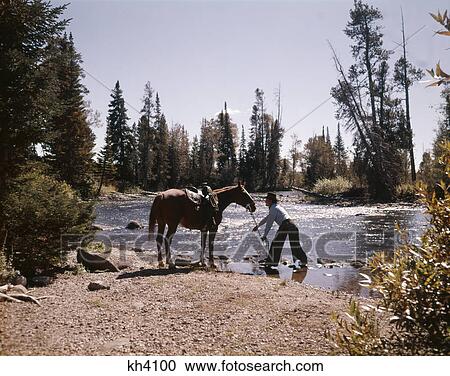 1970S Cowboy Standing In Stream Leading Horse By Reins To Water View Large Photo Image Stock Image - 1970S Cowboy Standing In Stream Leading Horse By Reins To Water. Fotosearch