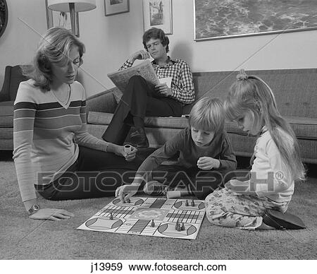 Stock Photo - 1970S Family Mother Kids Playing Board Game Living Room Floor Father Reading Newspaper. Fotosearch