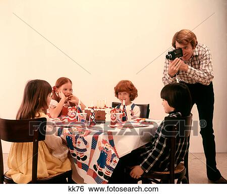 Stock Photograph - 1970S Father With Home Movie Camera Taking Pictures Birthday Party Children At Table . Fotosearch