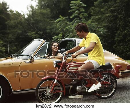 1970S Lifestyle Talking Flirt Couple Man On Small Red Harley Davidson Motorcycle Smiling Woman In Orange Porsche Automobile View Large Photo Image Stock Image - 1970S Lifestyle Talking Flirt Couple Man On Small Red Harley Davidson Motorcycle Smiling Woman In Orange Porsche Automobile. Fotosearch