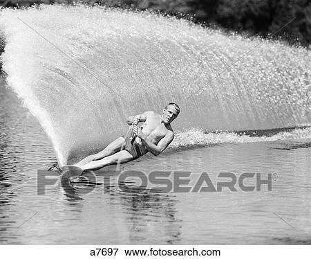 1970S Man Slalom Water Skiing Leaning To Side To Create Wall Of Water Behind View Large Photo Image Stock Photo - 1970S Man Slalom Water Skiing Leaning To Side To Create Wall Of Water Behind. Fotosearch