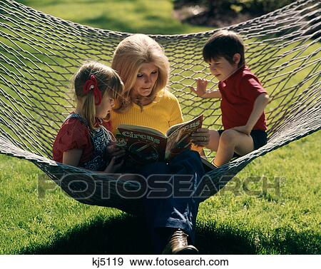 Stock Photo - 1970S Mother Son And Daughter Sitting In Hammock Reading A Book Outdoor . Fotosearch