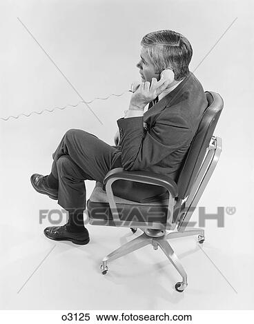 1970S Profile Executive Businessman Sitting In Office Chair Talking On Telephone View Large Photo Image Stock Photography - 1970S Profile Executive Businessman Sitting In Office Chair Talking On Telephone. Fotosearch