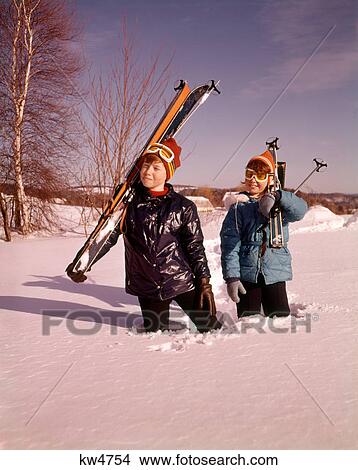 1970S Smiling Young Boy And Girl Walking In Deep Snow Up To Knees Carrying Skis And Ski Poles View Large Photo Image Picture - 1970S Smiling Young Boy And Girl Walking In Deep Snow Up To Knees Carrying Skis And Ski Poles . Fotosearch