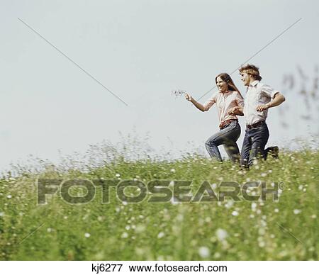 Stock Photo - 1970S Young Teen Couple Boy Girl Running Field Wildflowers. Fotosearch