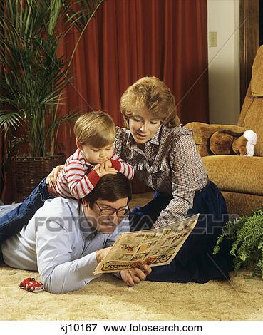 1980S Family On Living Room Floor Father Reading Newspaper Comics To Boy And Mother View Large Photo Image Stock Photo - 1980S Family On Living Room Floor Father Reading Newspaper Comics To Boy And Mother. Fotosearch