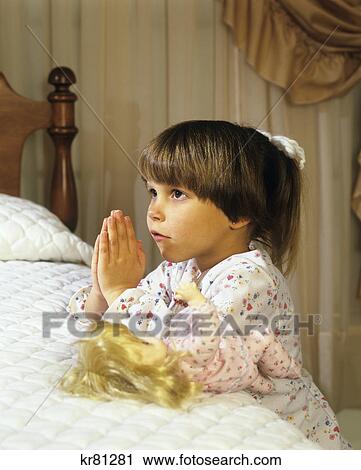 Stock Image - 1980S Girl Kneeling Beside Bed Saying Her Prayers . Fotosearch
