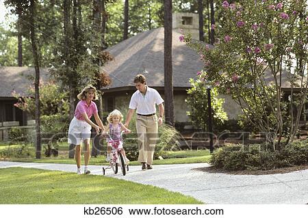 Stock Photograph - 1980S Parents Helping Child Ride New Bike. Fotosearch