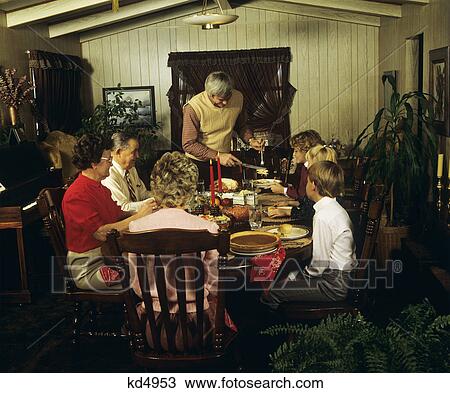Stock Image - 1980S Three Generation Family Thanksgiving Dinner Father Carving Turkey. Fotosearch