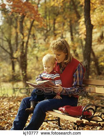 Stock Photo - 1980S Woman Reading Book To Toddler Sitting Autumn Park Bench. Fotosearch