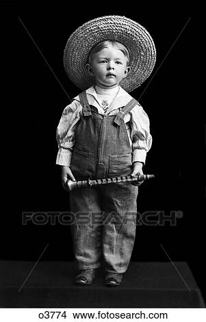 1800S 1890S Turn Of The Century Boy In Overalls & Straw Hat Holding Small Clarinet-Like Instrument View Large Photo Image Picture - 1800S 1890S Turn Of The Century Boy In Overalls & Straw Hat Holding Small Clarinet-Like Instrument. Fotosearch