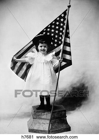 1890S Turn Of Century Smiling Little Girl Standing On Platform Wearing A White Dress And A Dark Hat Holding A American Flag View Large Photo Image Stock Image - 1890S Turn Of Century Smiling Little Girl Standing On Platform Wearing A White Dress And A Dark Hat Holding A American Flag. Fotosearch