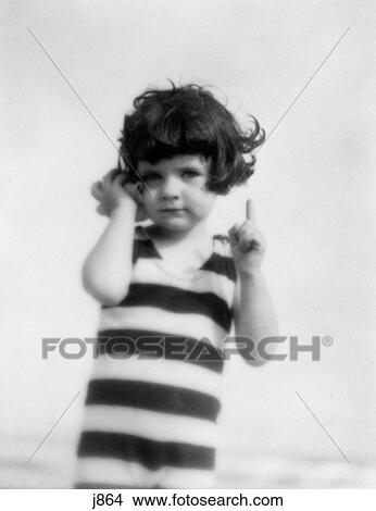 Picture - 1920S Girl In Striped Bathing Suit Holding Seashell Up To Ear. Fotosearch