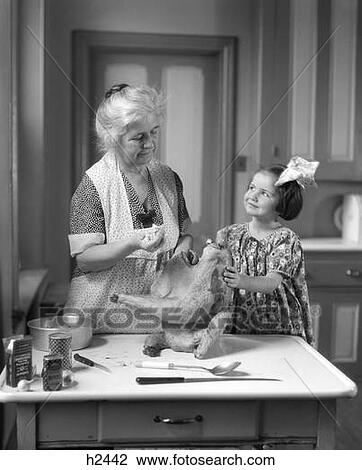 Stock Image - 1920S Little Girl Helping Grandmother Stuff Turkey. Fotosearch