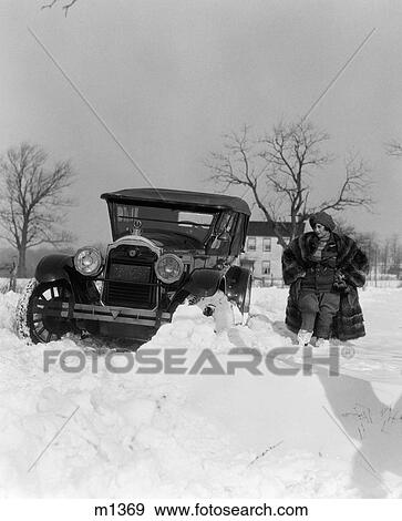 Stock Photo - 1920S Packard Stuck In Snow Bank With Woman In Jodhpurs And Open Fur Coat Sizing Up The Situation . Fotosearch