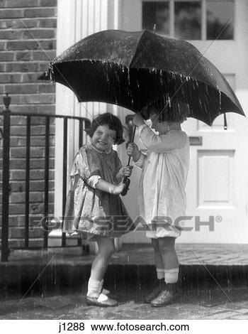 Stock Photo - 1920S Pair Of Little Girls Standing On Front Stoop Under Umbrella In Pouring Rain. Fotosearch