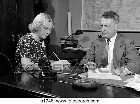 1930S 1940S Businessman Sitting At Desk Going Over Paperwork With Secretary Taking Dictation Man Woman Office Indoor View Large Photo Image Stock Photograph - 1930S 1940S Businessman Sitting At Desk Going Over Paperwork With Secretary Taking Dictation Man Woman Office Indoor. Fotosearch