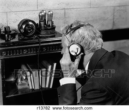 Stock Image - 1930S 1940S Elderly Man Listening To Crystal Radio Through Headphones. Fotosearch