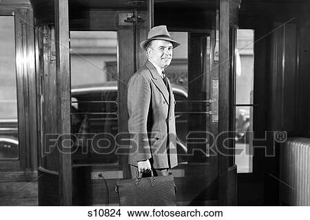 1930S 1940S Smiling Businessman In Hat Double Breasted Suit Briefcase Leaving Building Through Revolving Door Looking At Camera View Large Photo Image Picture - 1930S 1940S Smiling Businessman In Hat Double Breasted Suit Briefcase Leaving Building Through Revolving Door Looking At Camera. Fotosearch